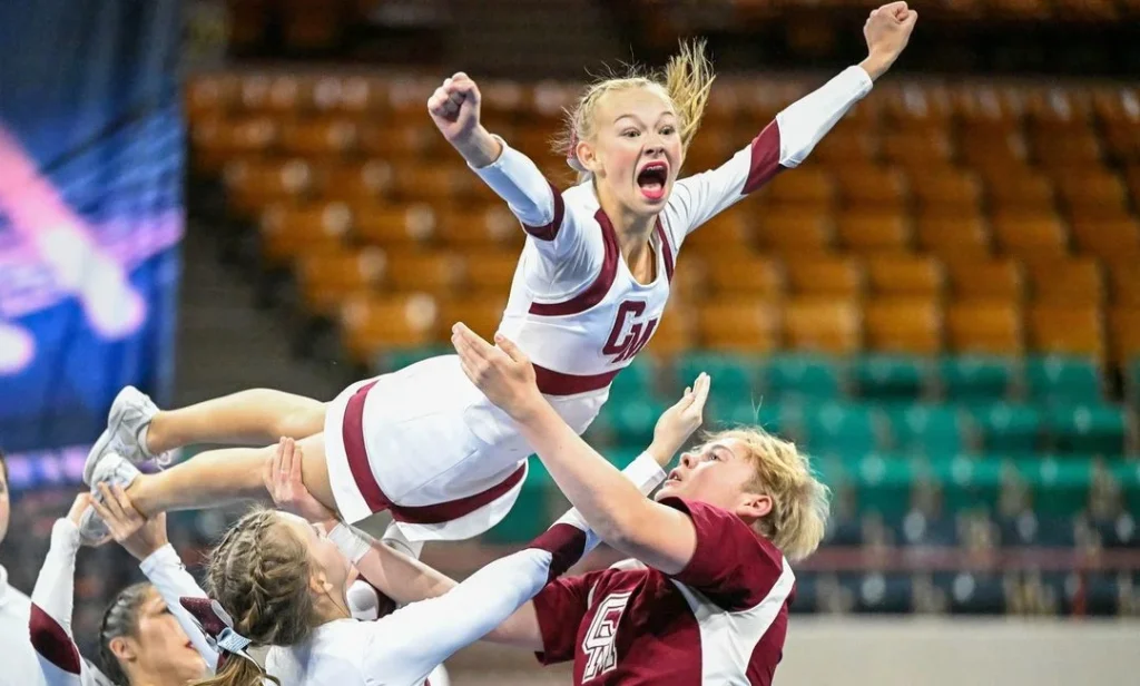 girl doing cheer photo poses while doing a stunt with her cheerleading team