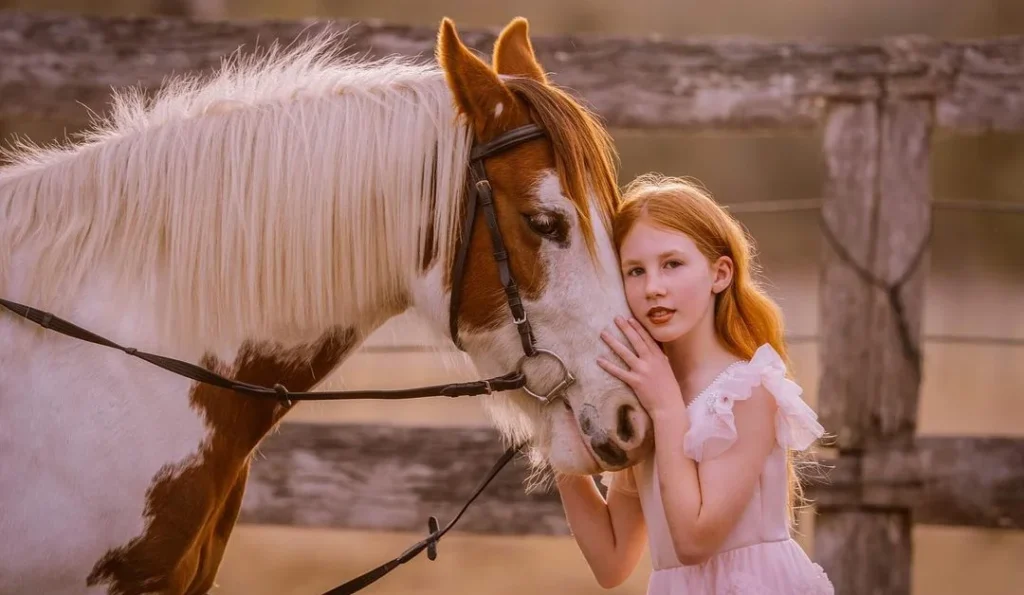 little girl with red hair posing with her horse face on face in the golden hour for horse photography