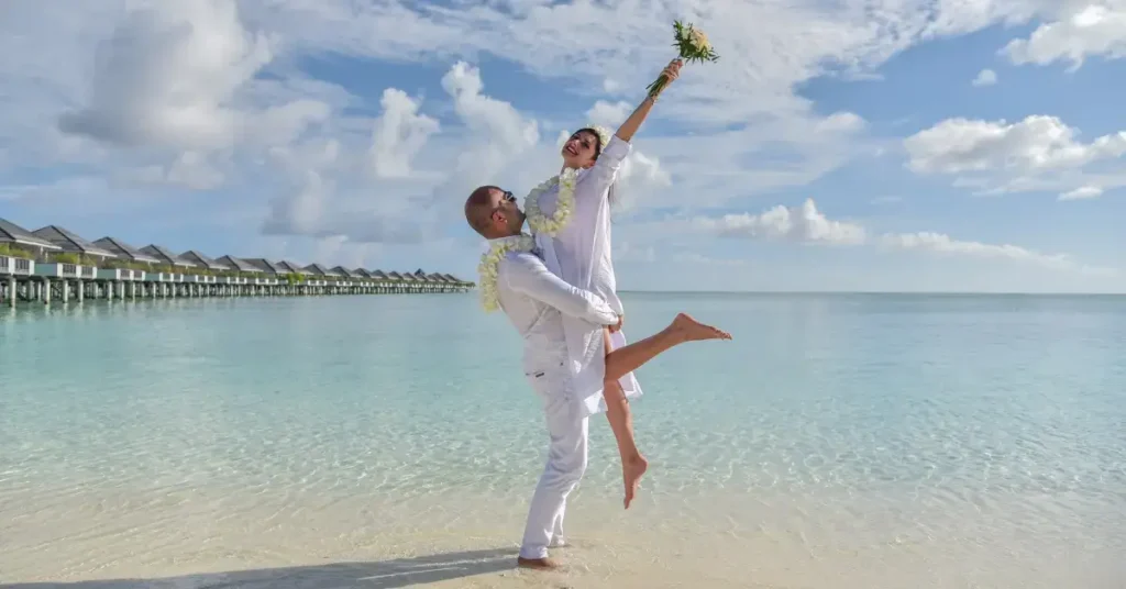 wedding photography at the beach with a woman holding flowers into the sky next to the sea