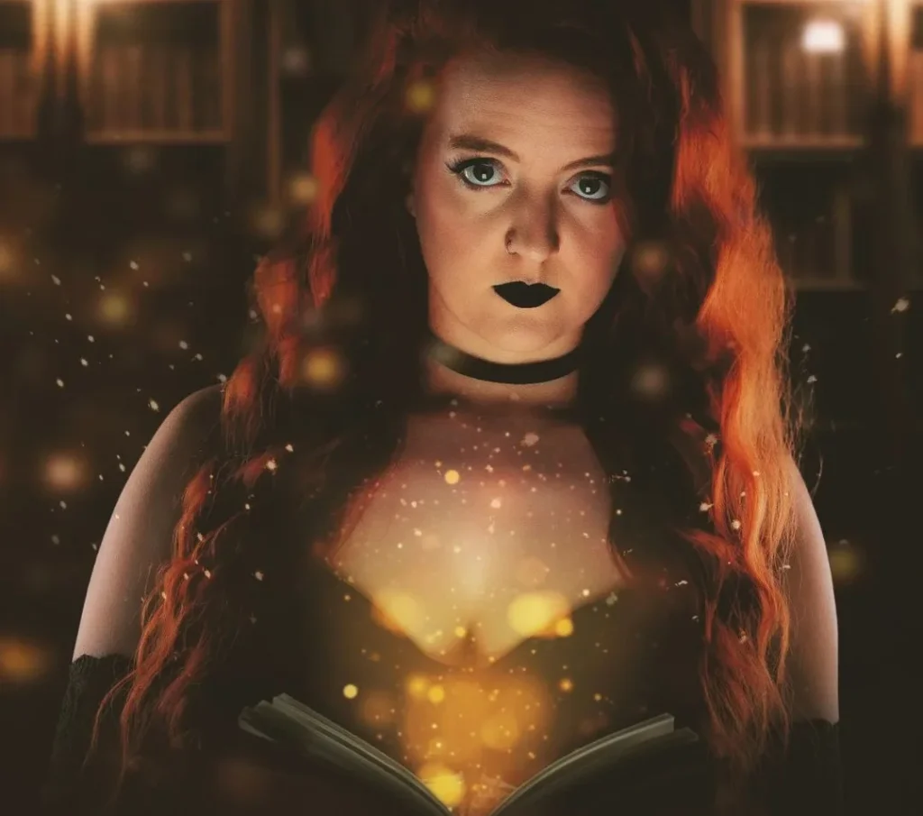 witch holding a book with golden sparkles while looking in the camera at a witchy photosession