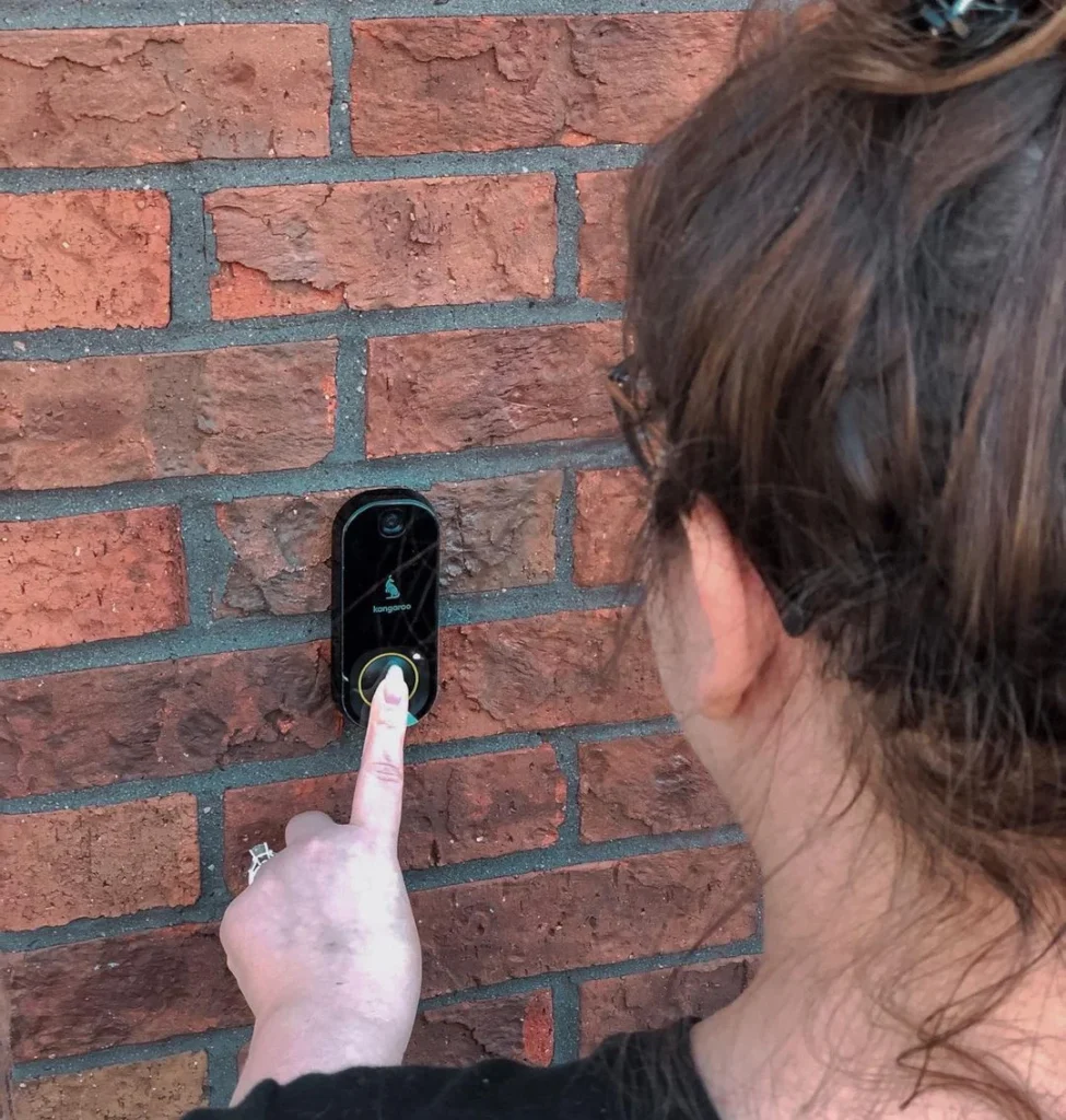 woman ringing at a doorbell camera from amazon on a brick wall, video camera doorbell