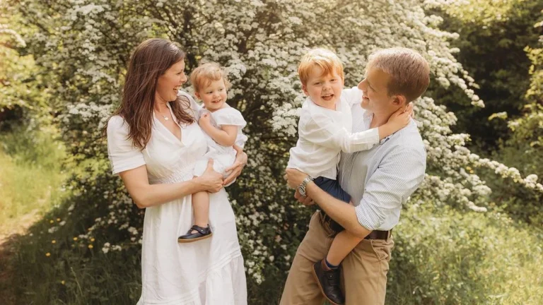 happy family posing for a spring family photoshoot outdoors in front of blossoming flowers and trees, joyful family photo